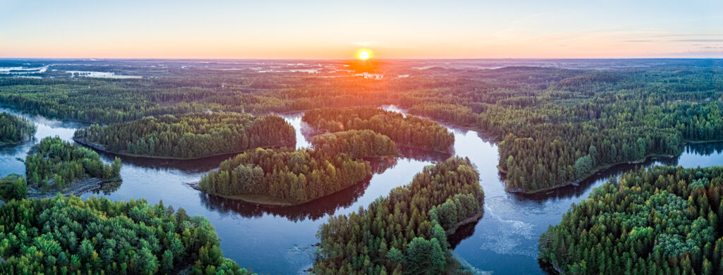 Laajakuva järvimaisemasta, jossa aurinko on juuri laskemassa horisonttiin.