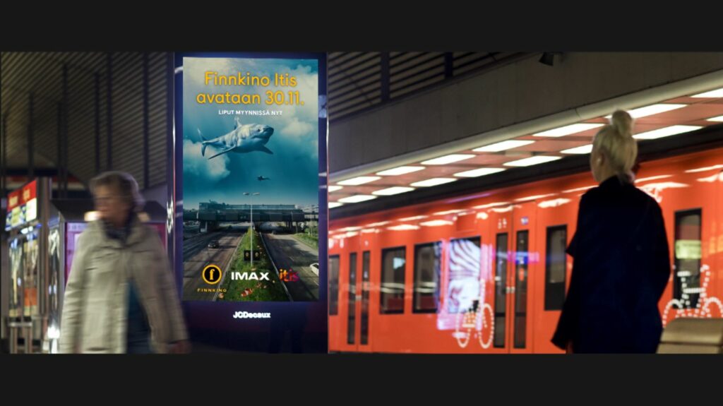 Metroasemalla mainoskyltti, jossa mainos Itikseen avautuvasta Finnkinosta. Taustalla metro.
