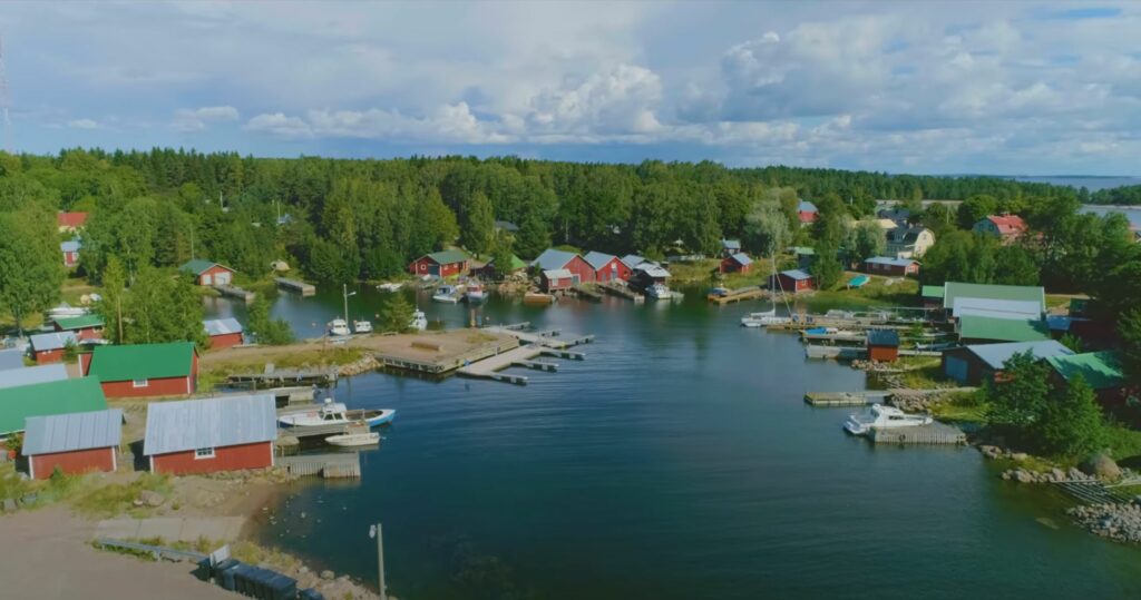 Kesäinen maisemakuva venesatamasta, jossa paljon punaisia taloja ja puita.