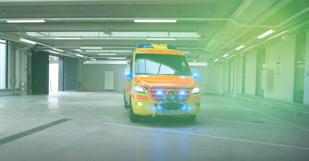 Ambulanssi parkkihallissa, valot päällä.